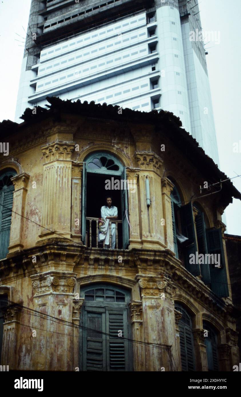 Vista di una vecchia casa d'angolo a Singapore. La facciata è scappare e scolorita. Il tetto è parzialmente rotto. Nella finestra superiore c'è una persona. Sullo sfondo un moderno ed alto edificio. [traduzione automatica] Foto Stock
