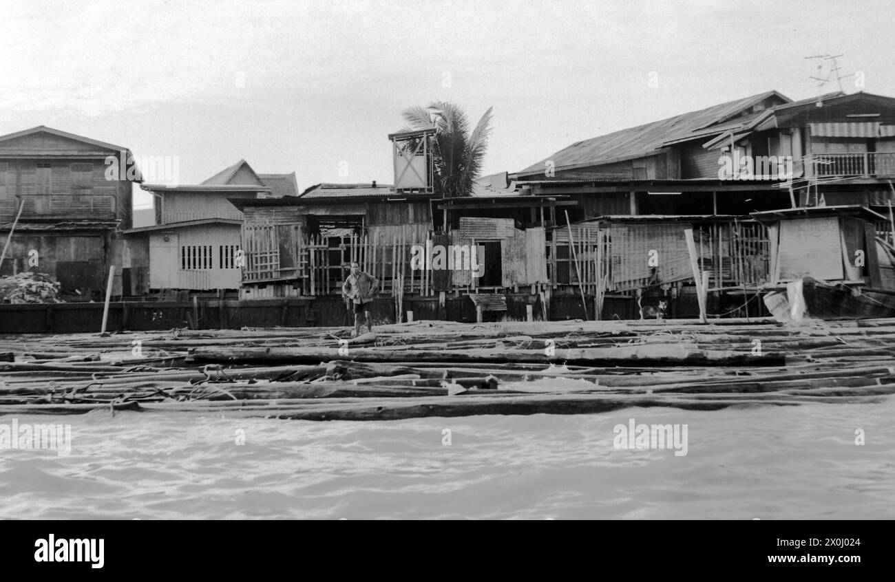 Vista della riva del fiume Chao Phraya a Bangkok, Thailandia nel giugno 1972. Un uomo è in piedi sulla banca. Dietro di lui ci sono capanne di legno e case in più file. Alcuni di loro si levano in piedi sui palafitte. [traduzione automatica] Foto Stock