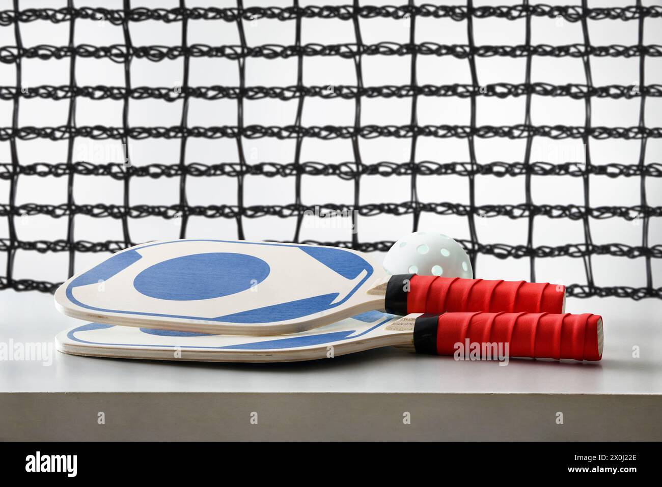 Due racchette da picchetto blu e rosso e una palla bianca su un tavolo bianco isolato con una rete di gioco sullo sfondo. Vista frontale. Foto Stock