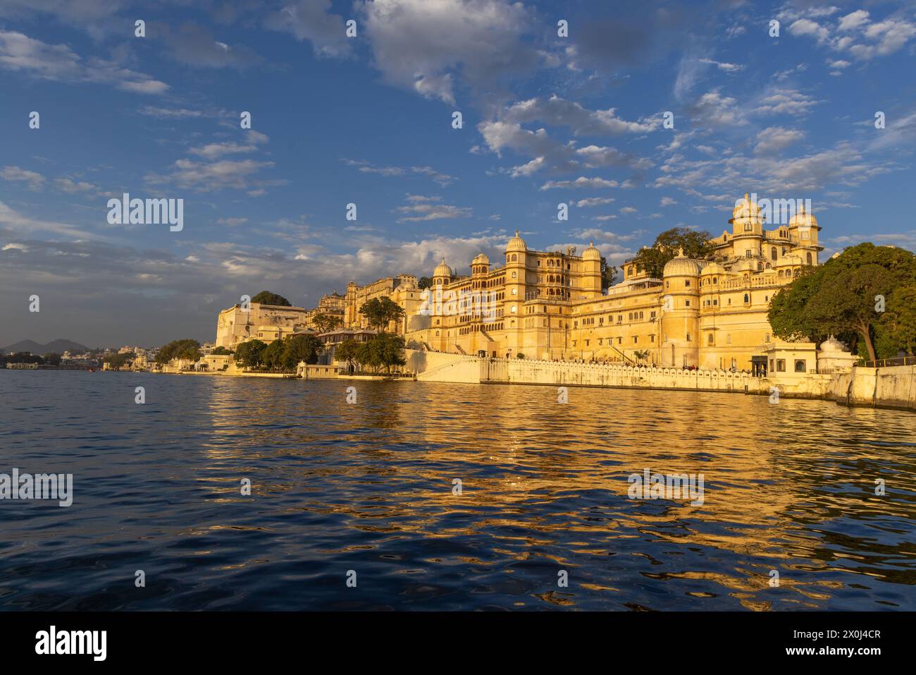 Il Palazzo della città di Udaipur è illuminato dalla luce dorata del sole, come si vede mentre si va in barca sul lago Pichola Foto Stock