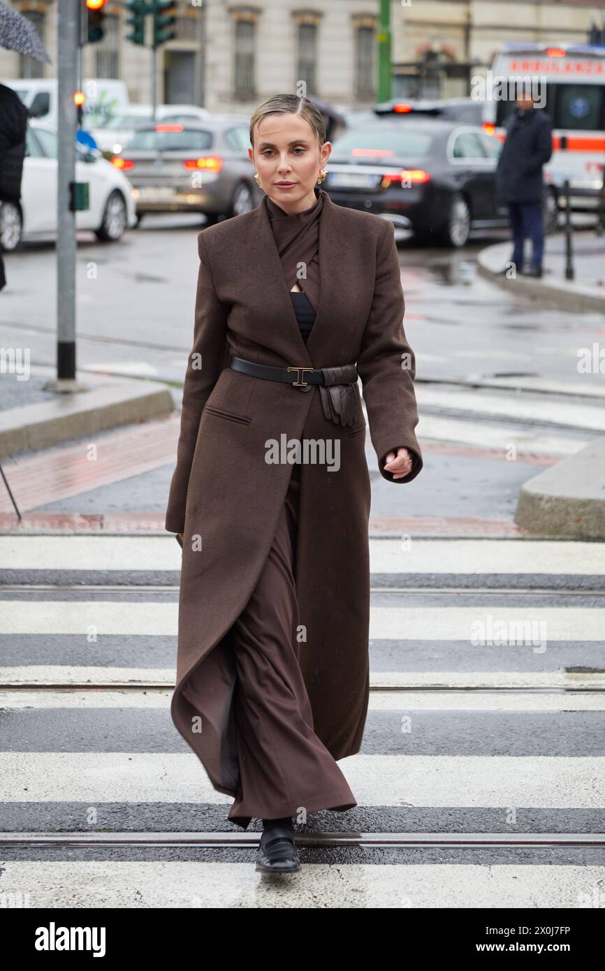 MILANO, ITALIA - 23 FEBBRAIO 2024: Donna con cappotto lungo marrone e cintura Tods prima della sfilata di moda Tods, Milano Fashion Week Street style Foto Stock