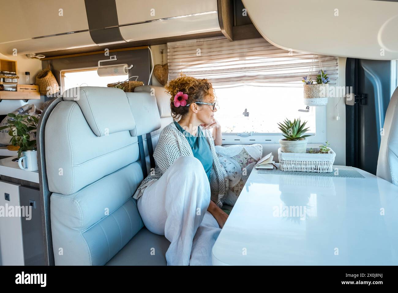 Vanlife, lo stile di vita delle persone. Una giovane donna adulta si rilassa sul divano di un camper moderno e accogliente e guarda fuori dalla finestra. Viaggi persone e stile di vita. Noleggio di un camper per per le vacanze Foto Stock