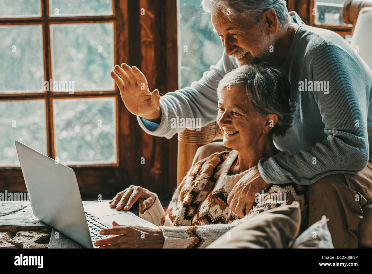 Felice coppia senior uomo e donna che fanno videochiamata con il portatile a casa seduto sul pavimento e sedia insieme avendo un. Gesto Hallo e persone mature moderne con tecnologia di connessione per il tempo libero Foto Stock