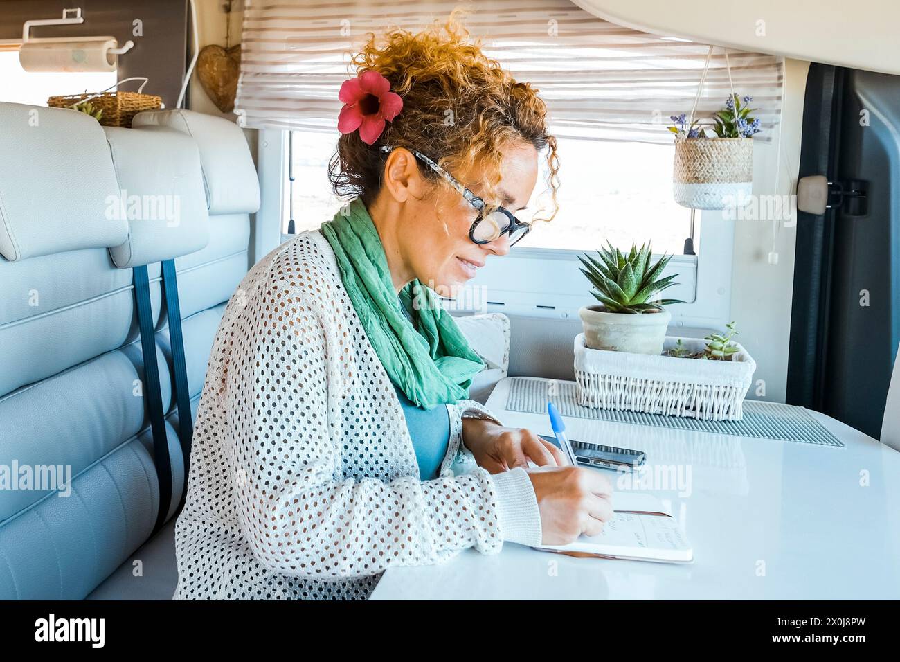 Una donna seduta all'interno di un moderno camper alternativa una piccola casa e scrivere appunti di viaggio sul tavolo. Persone che vivono vanlife sulla strada, vita e vacanza. Viaggiatore donna attività ricreative al coperto Foto Stock