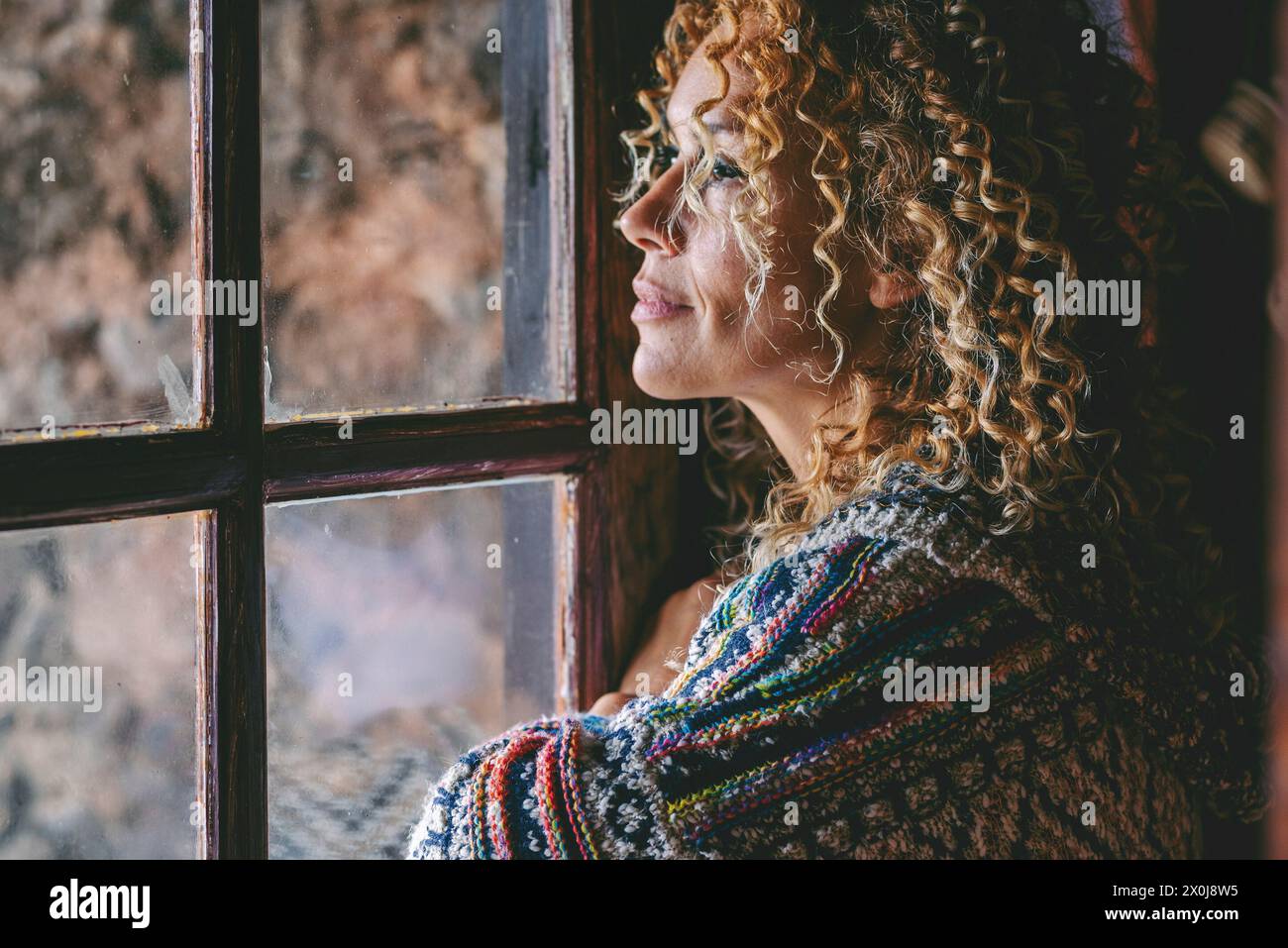 Una donna sola in piedi a casa vicino alla finestra che guarda fuori e pensa. Stile di vita femminile single. Amici e pensieri in attesa. Young lady per il tempo libero al coperto. Ritratto laterale di mezza età Foto Stock