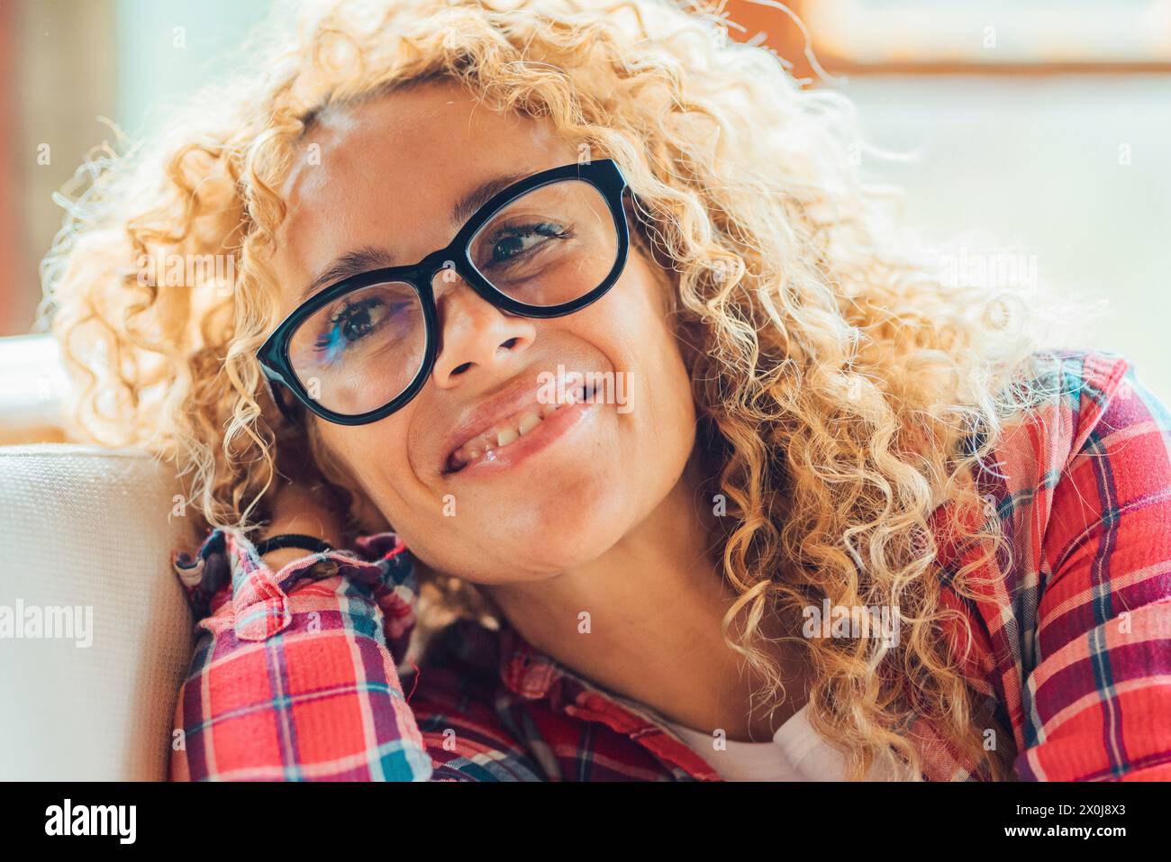 Allegro giovane adulto bella donna di mezza età ritratto di occhiali che si diverte e sorride a casa in un luminoso salotto. Le donne felici amano rilassarsi al chiuso sul divano e indossare gli occhiali da vista Foto Stock