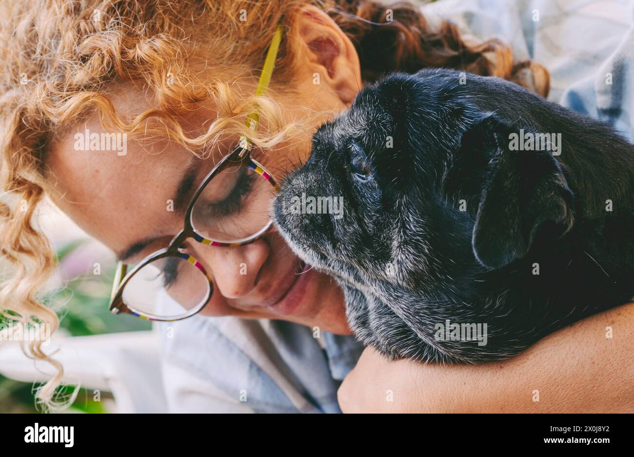 Amate il concetto di persone e cani animali con una donna caucasica adulta felice e un vecchio cucciolo nero che abbraccia e ama i tendini insieme. Il concetto dei migliori amici per sempre Foto Stock