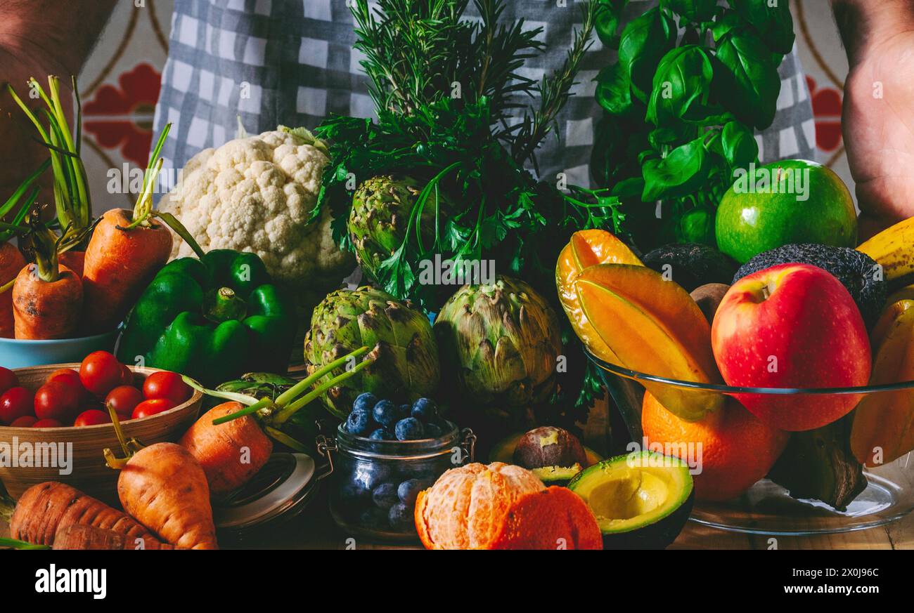 L'inconfondibile chef uomo mostra i suoi prodotti freschi di stagione di frutta e verdura sul tavolo a casa o al ristorante. Insalata ingredienti di stile di vita sano per la perdita di peso piano nutrizionale Foto Stock