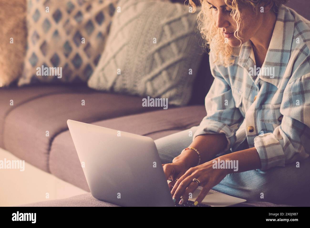Donna moderna che lavora online con un computer portatile comodamente seduto sul divano di casa. Concetto di smart working lifestyle femminile. Donna che usa il notebook e si rilassa Foto Stock