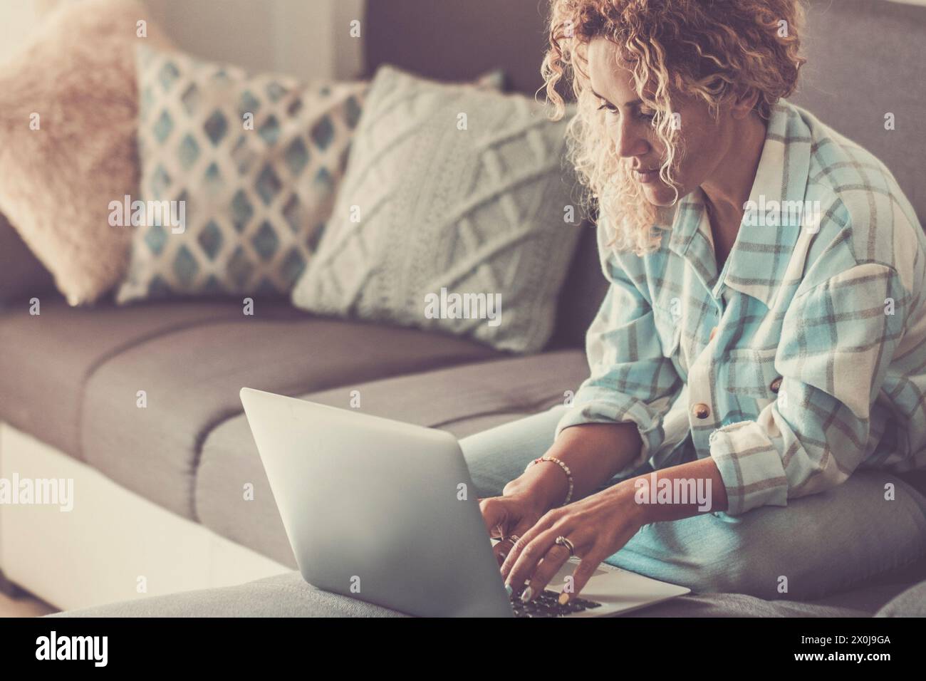 Una donna adulta che usa un computer portatile sul divano. Attività di svago online con tecnologia indoor. Donne moderne che vivono da sole e comunicano con un computer con connessione wireless. Donna intelligente che lavora con stile Foto Stock