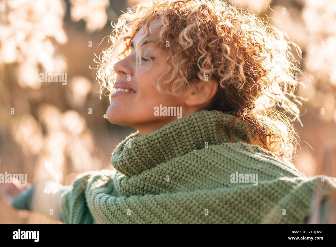 Una donna di bellezza con un'espressione felice e idilliaca sul braccio che si apre sul viso e si gode la luce del tramonto sul campo durante una scenografica attività di svago all'aperto. Persone che amano la vita e il concetto di stile di vita sano. Vita Foto Stock