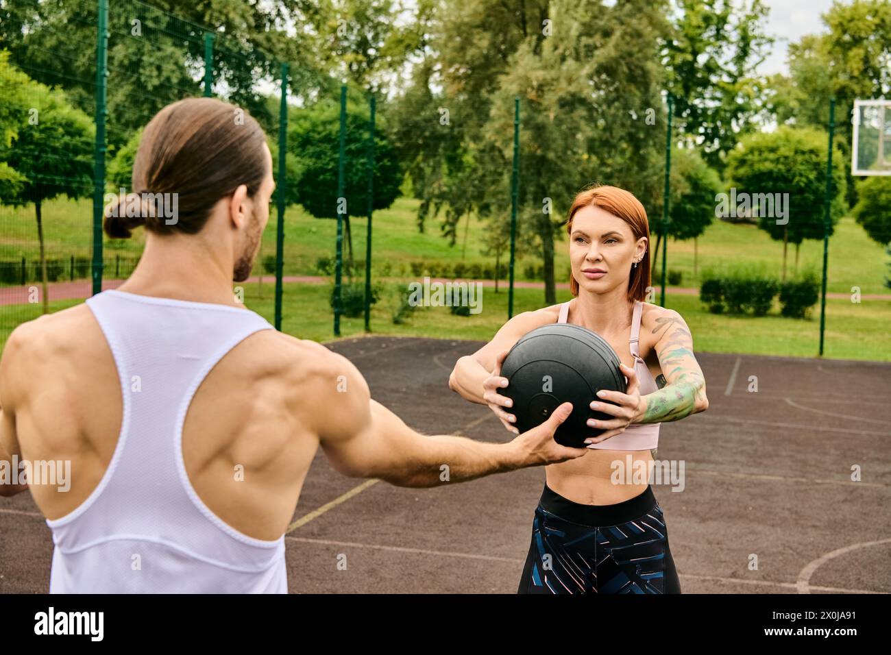 Una donna determinata tiene una palla mentre si trova accanto a un uomo in abbigliamento sportivo, mostrando la sua dedizione all'esercizio fisico. Foto Stock