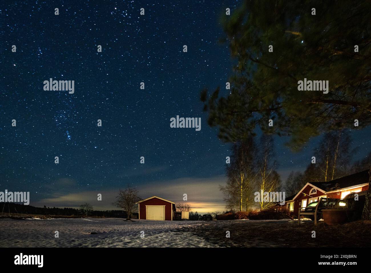 La via Lattea nel cielo azzurro direttamente sopra una casa rossa svedese in legno e gli alberi nel giardino all'inizio dell'inverno con neve e ghiaccio. Fengersfors, Svezia Foto Stock