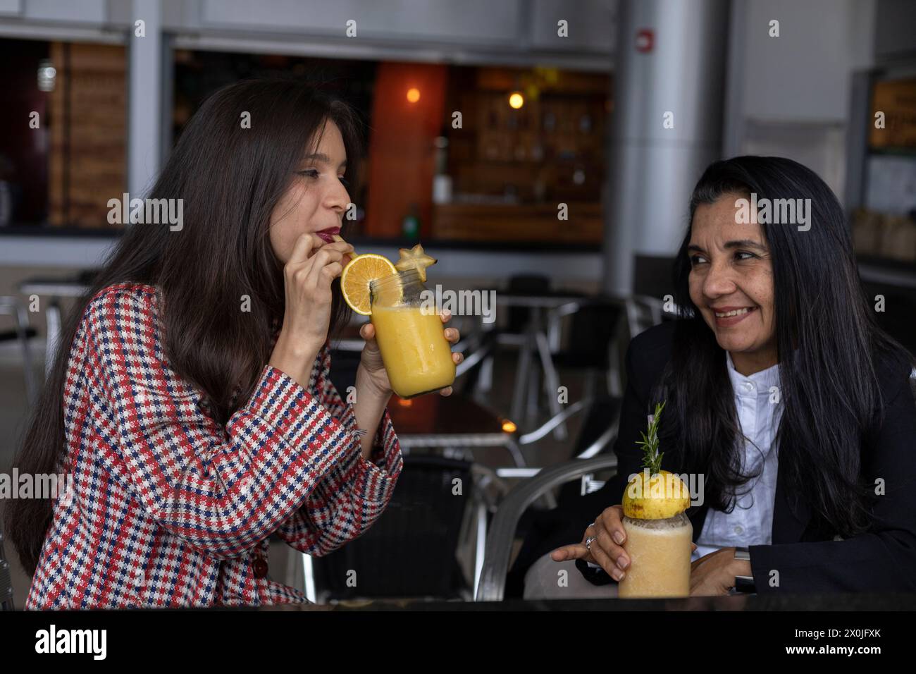 La mamma e la figlia latinoamericana chiacchierano, festeggiano e condividono un drink di frutta insieme. Festa della mamma e concetti di vita sana Foto Stock