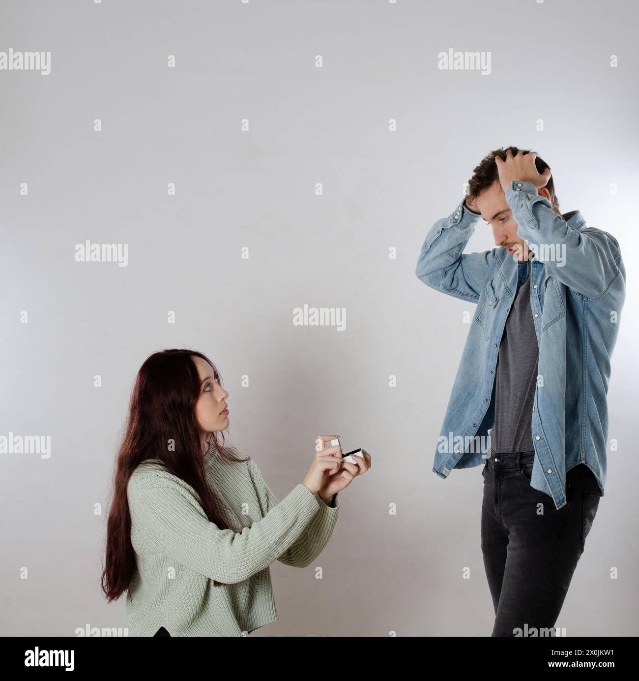 Donna in ginocchio che propone il matrimonio con il suo fidanzato con un anello in mano e lui è sorpreso Foto Stock
