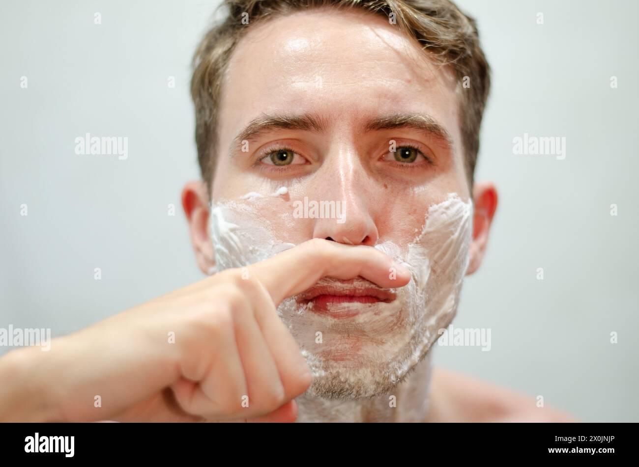 Bell'uomo caucasico che finge di avere i baffi con il dito davanti allo specchio. Concetto Movember. Foto Stock