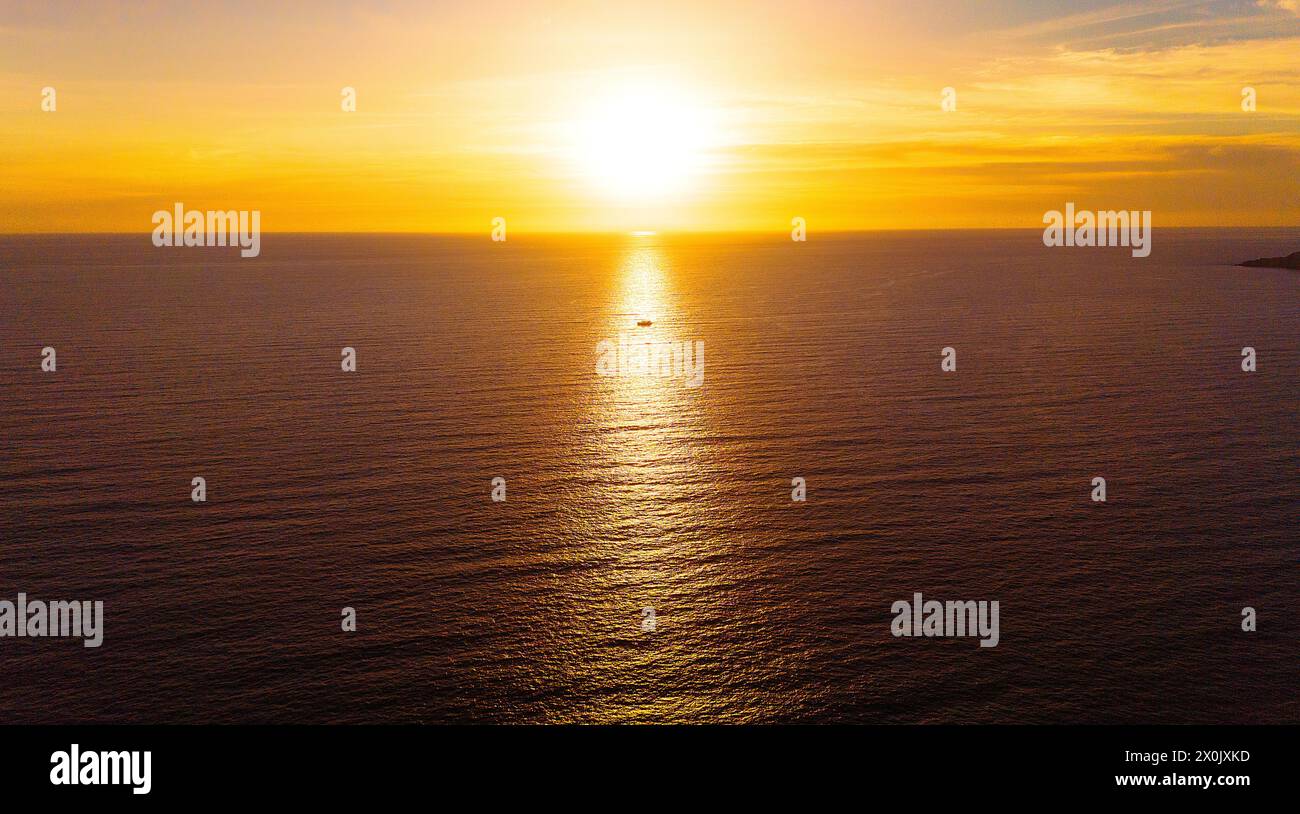 Un Seascape mozzafiato mentre il Sole scende sotto l'orizzonte, gettando un sentiero d'oro attraverso il vasto oceano. In mezzo alla Maestà della natura, un piccolo vascello Sails. Foto Stock