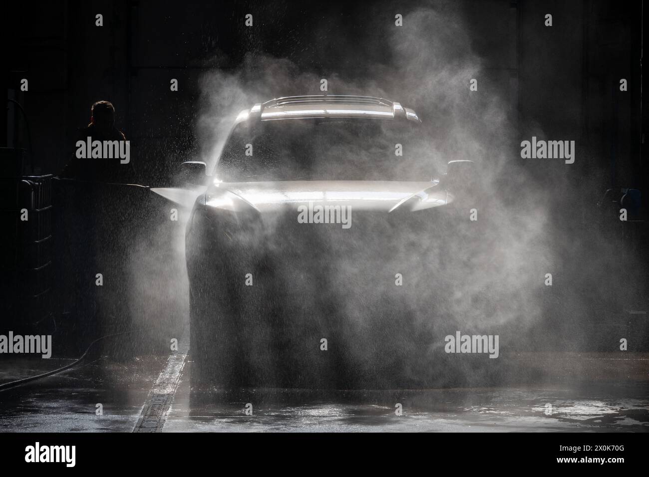 Osserva la silhouette di una persona che lava un'auto con un getto d'acqua in un centro di assistenza auto. La scena viene illuminata dalla retroilluminazione, evidenziando l Foto Stock