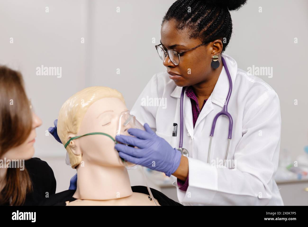 Un medico donna sta esaminando attentamente la testa di un manichino, praticando probabilmente procedure mediche o dimostrando tecniche in un ambiente clinico Foto Stock