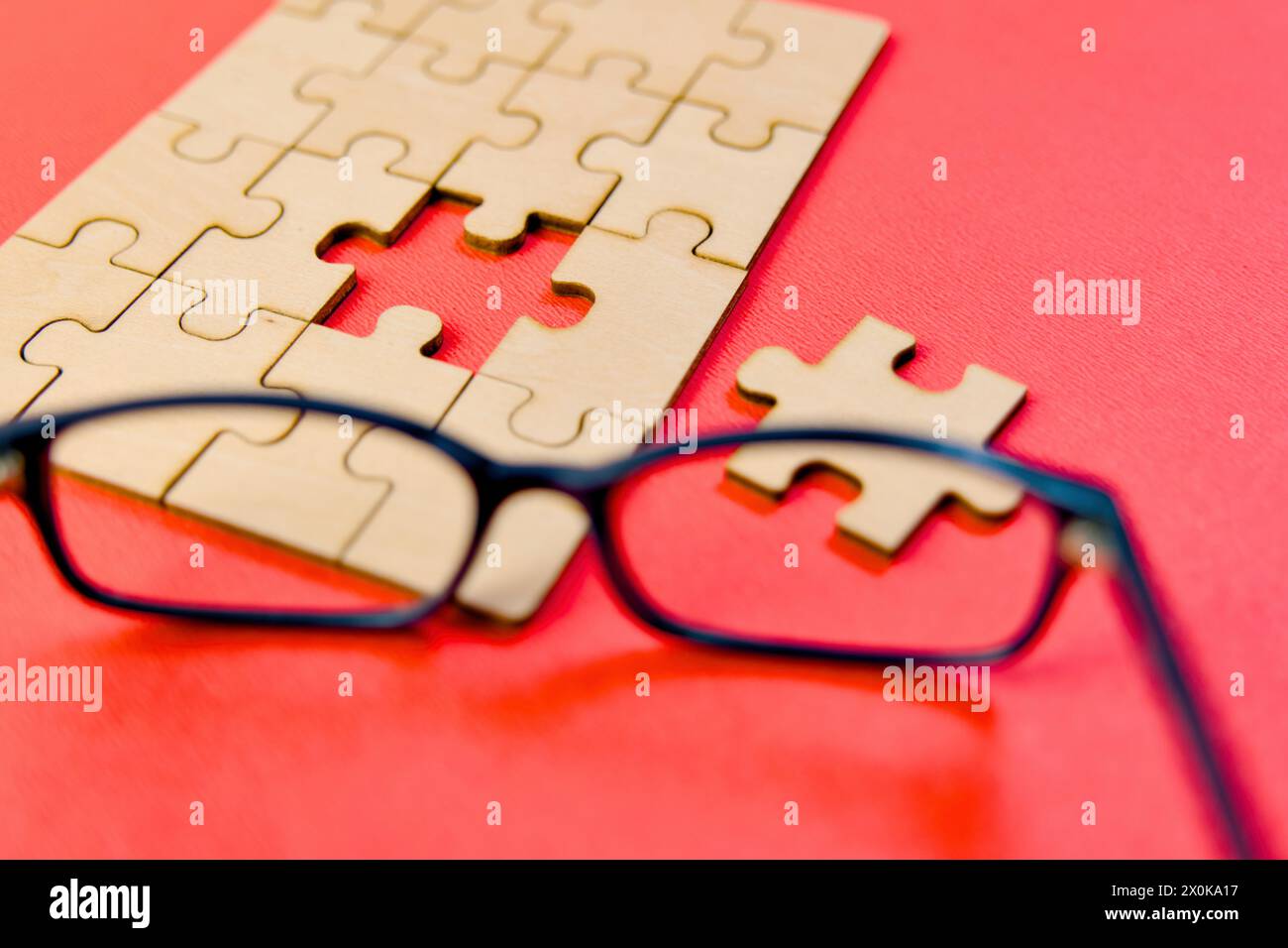 Questa immagine raffigura un paio di occhiali che poggiano accanto a un puzzle parzialmente completato su una superficie rossa Foto Stock