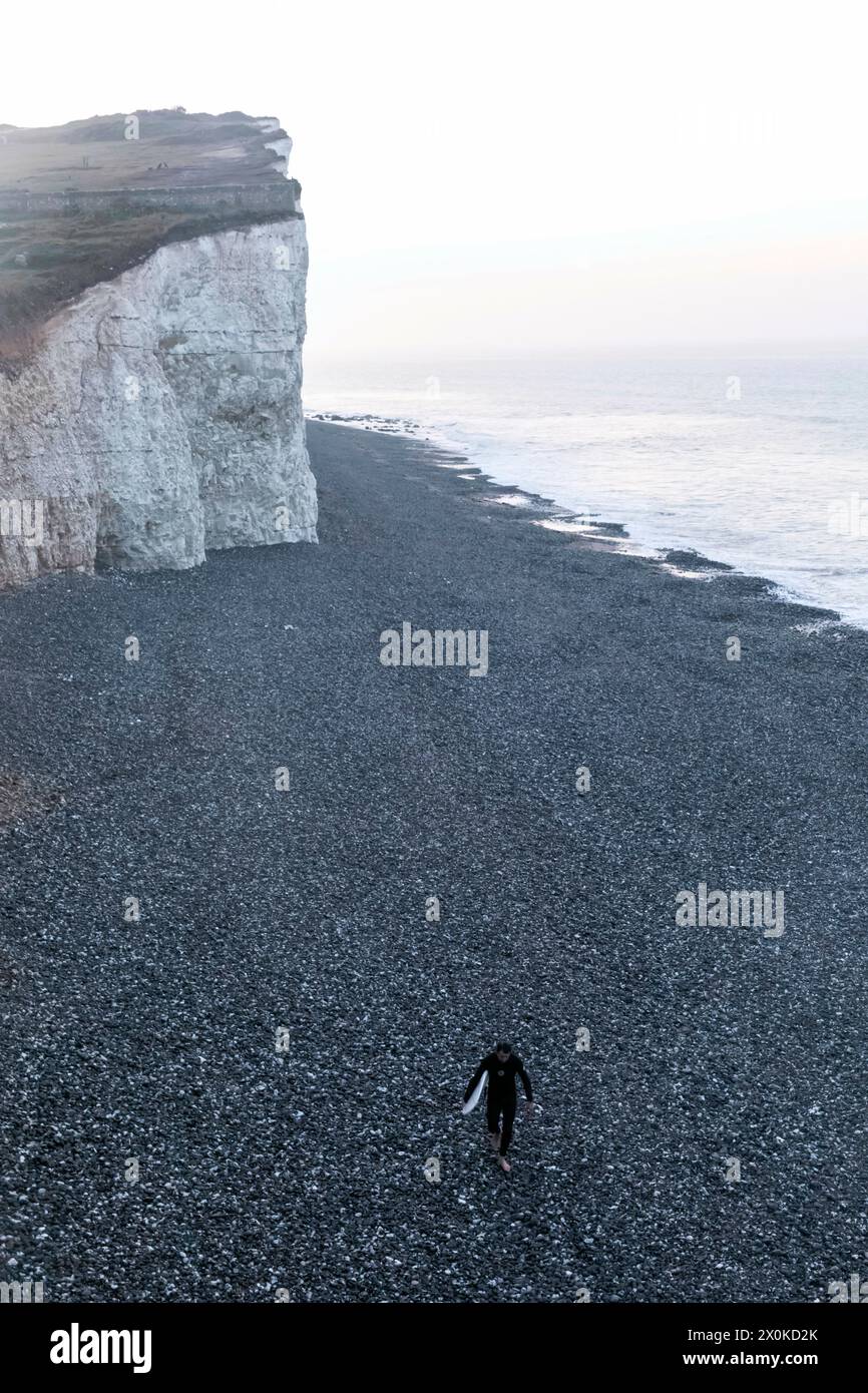Inghilterra, East Sussex, Eastbourne, South Downs National Park, Man Walking on Beach con tavola da surf a Burling Gap Foto Stock