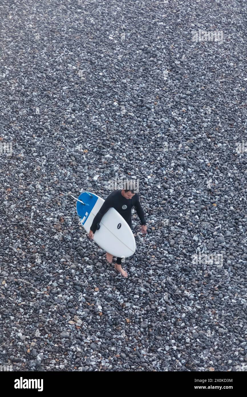 Inghilterra, East Sussex, Eastbourne, South Downs National Park, Man Walking on Beach con tavola da surf a Burling Gap Foto Stock