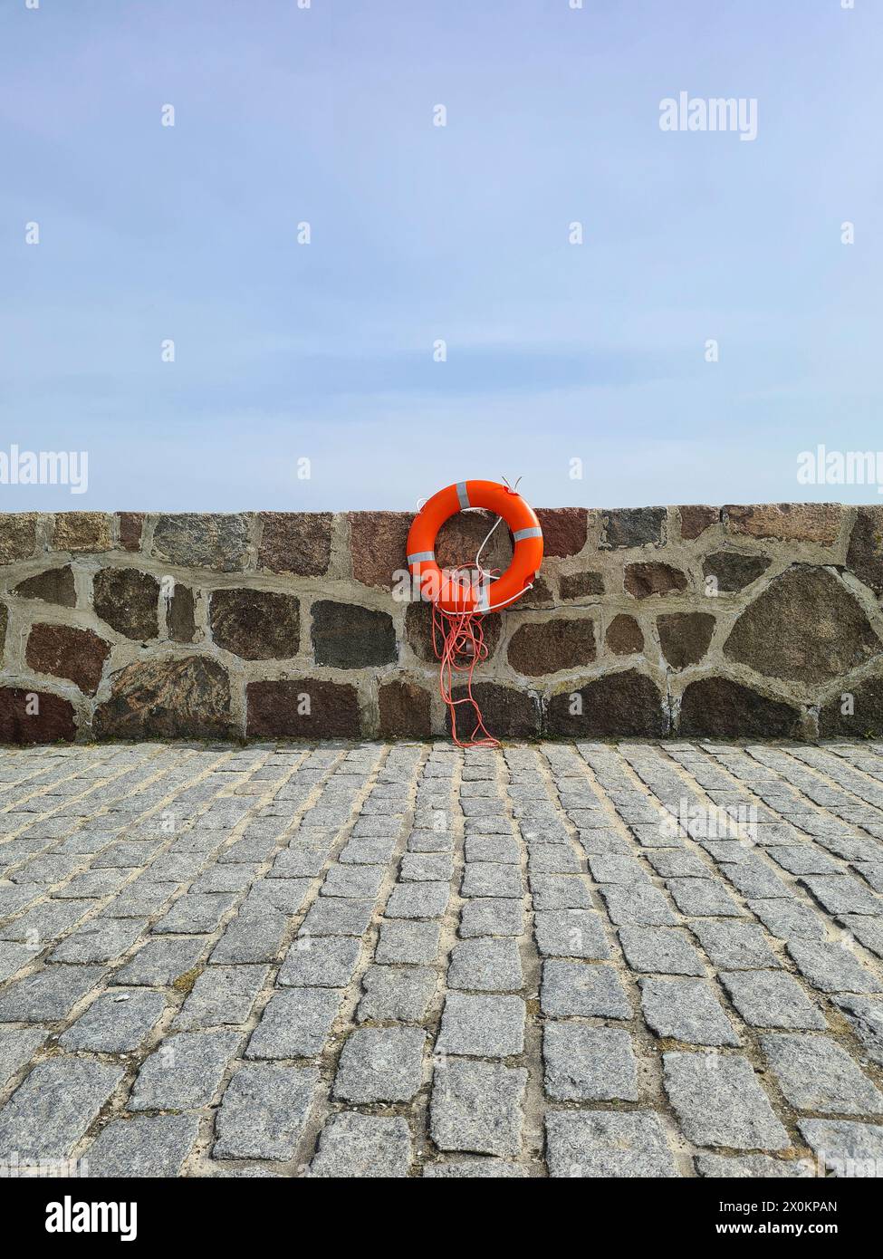 Un salvagente rosso con strisce riflettenti e un salvagente appeso su un muro di banchina, porto della città di Sassnitz, Germania Foto Stock