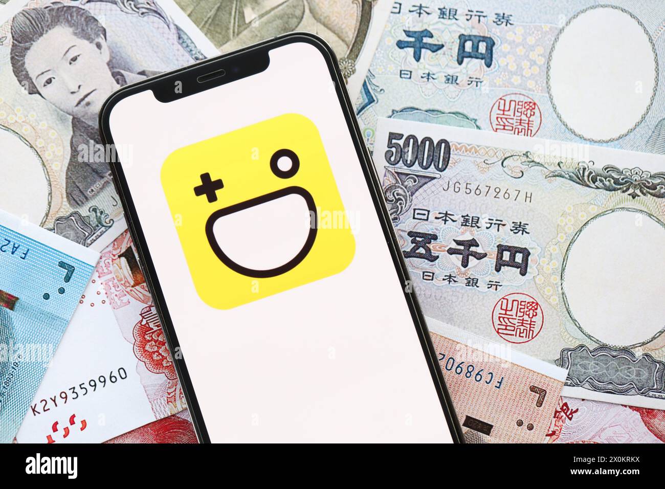 KIEV, UCRAINA - 1 APRILE 2024 icona Hago sullo schermo dello smartphone su molte banconote asiatiche. Display iPhone con logo app con banconote in yen giapponesi e yuan cinesi Foto Stock