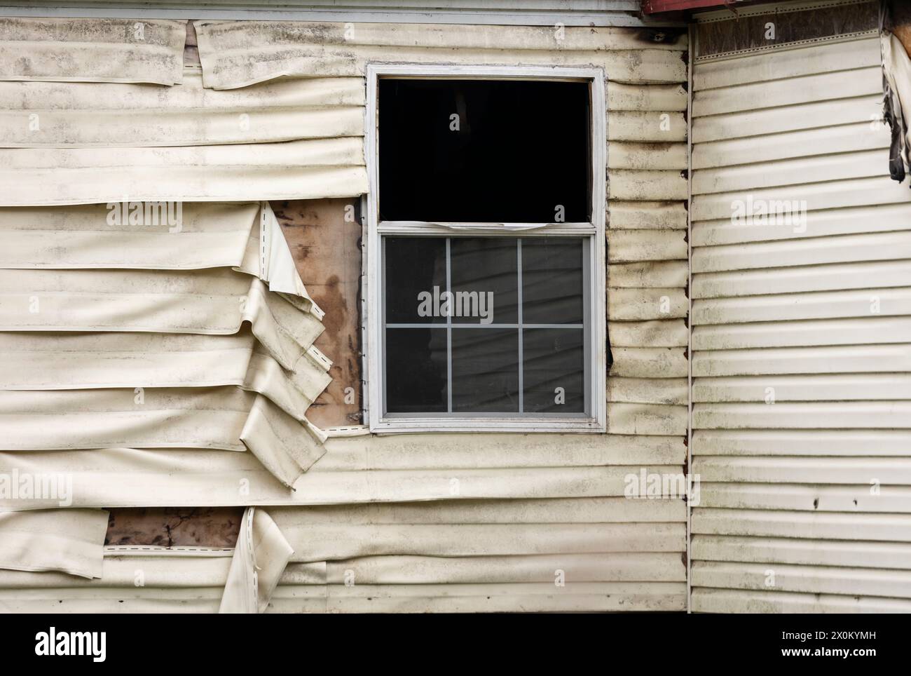 Una finestra esterna aperta con un rivestimento in vinile in plastica fuso e danneggiato ricoperto di fuliggine sporca su un'abitazione con una struttura residenziale interna calda Foto Stock