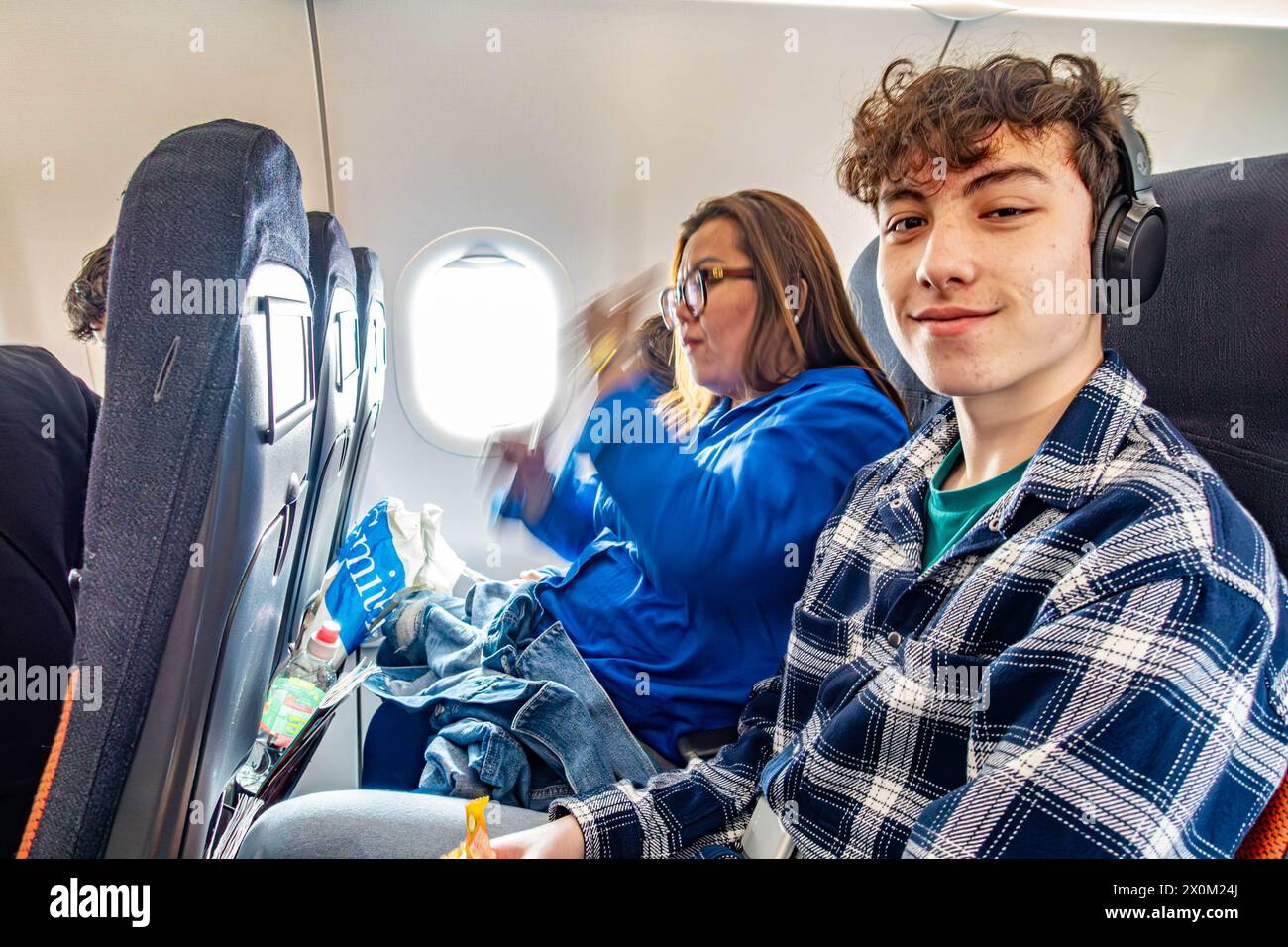 Una famiglia siede insieme a bordo di un aereo, un volo easyJet. Un adolescente si siede accanto alla sua mamma e sorride per la telecamera Foto Stock