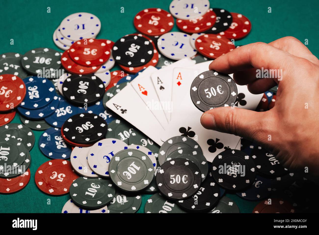 quattro di un genere di assi su una pila di chip da gioco sul tavolo verde nel primo piano del casinò. Concentrati sulla mano del giocatore con un chip nelle dita Foto Stock