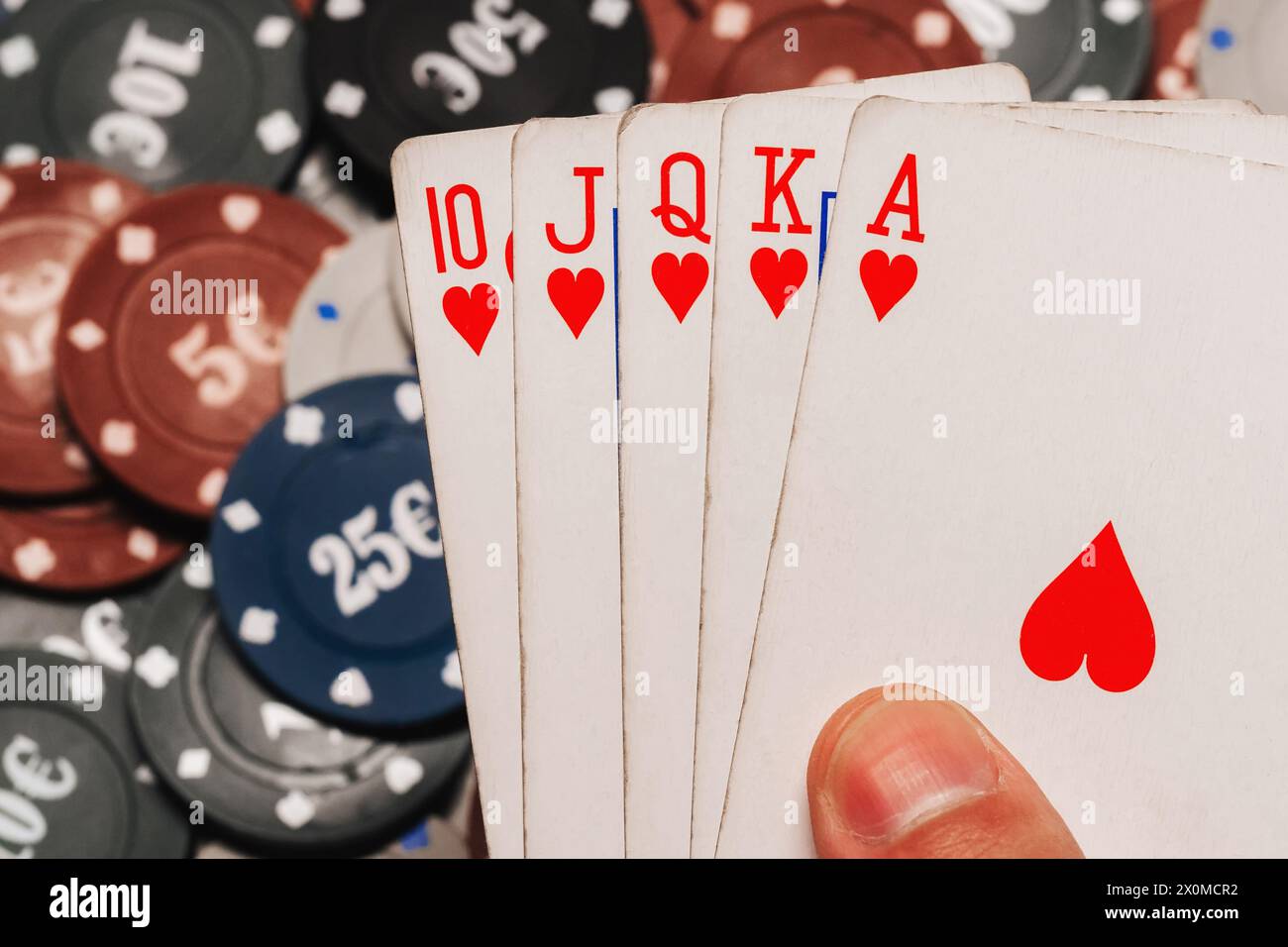 Royal Flush in poker nelle mani del giocatore sullo sfondo di chip di gioco nel primo piano del casinò Foto Stock