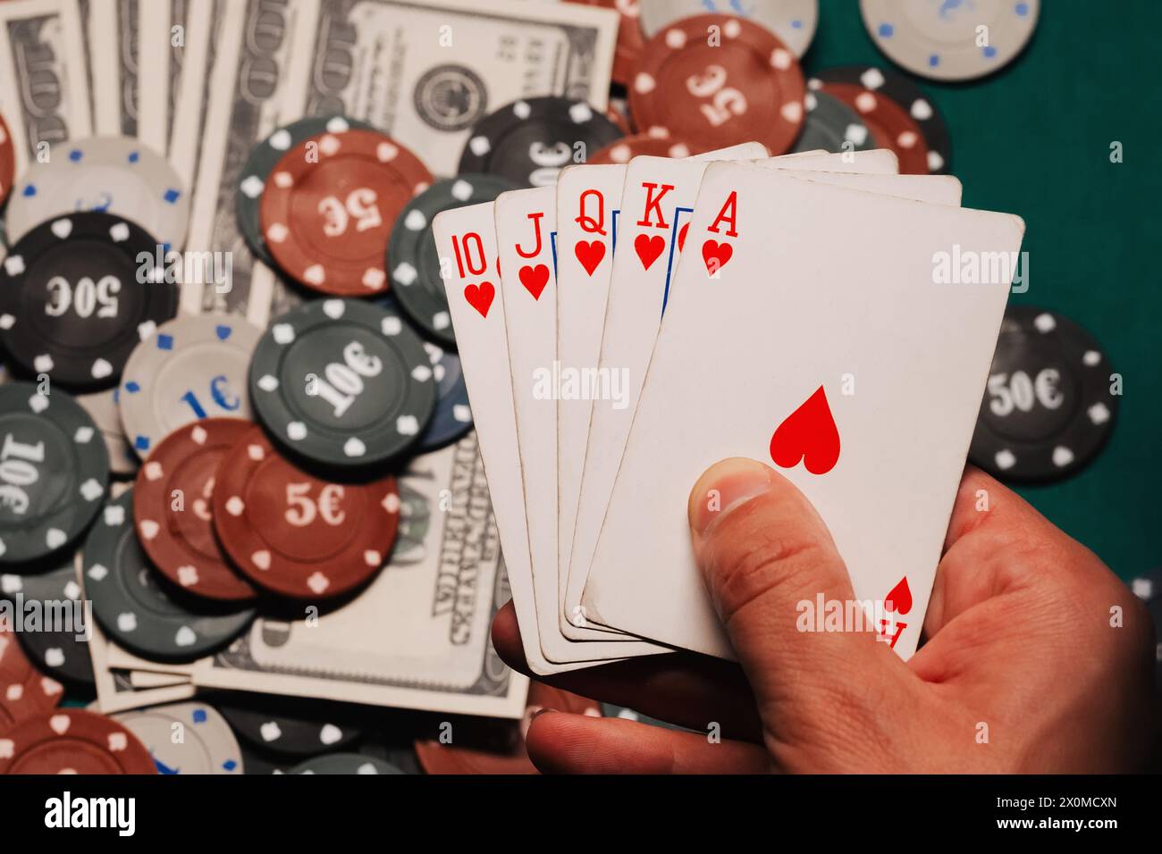 Royal Flush in poker nelle mani del giocatore sullo sfondo di chip di gioco e soldi nel primo piano del casinò Foto Stock