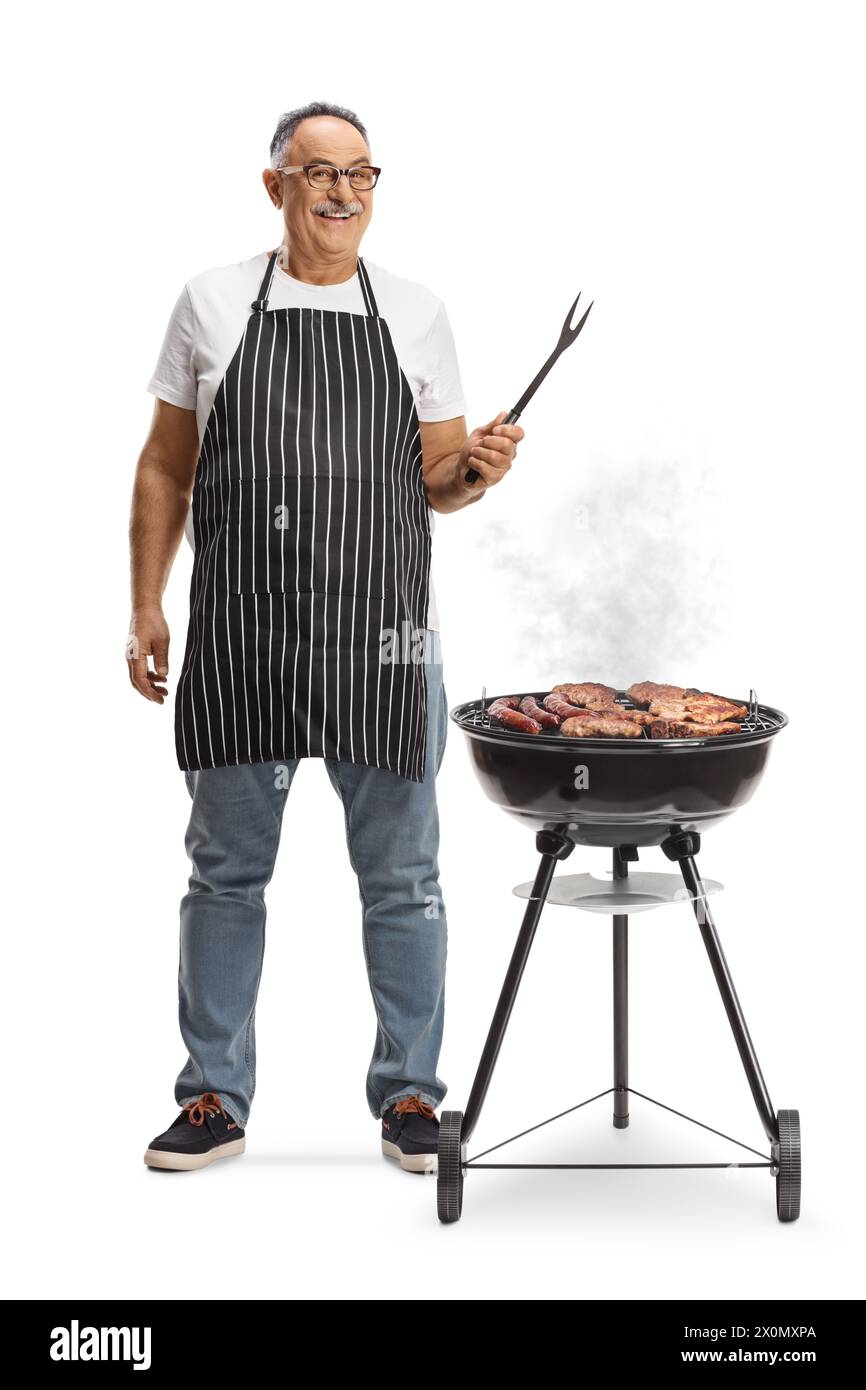 Uomo maturo accanto a un barbecue portatile che tiene una forchetta isolata su sfondo bianco Foto Stock