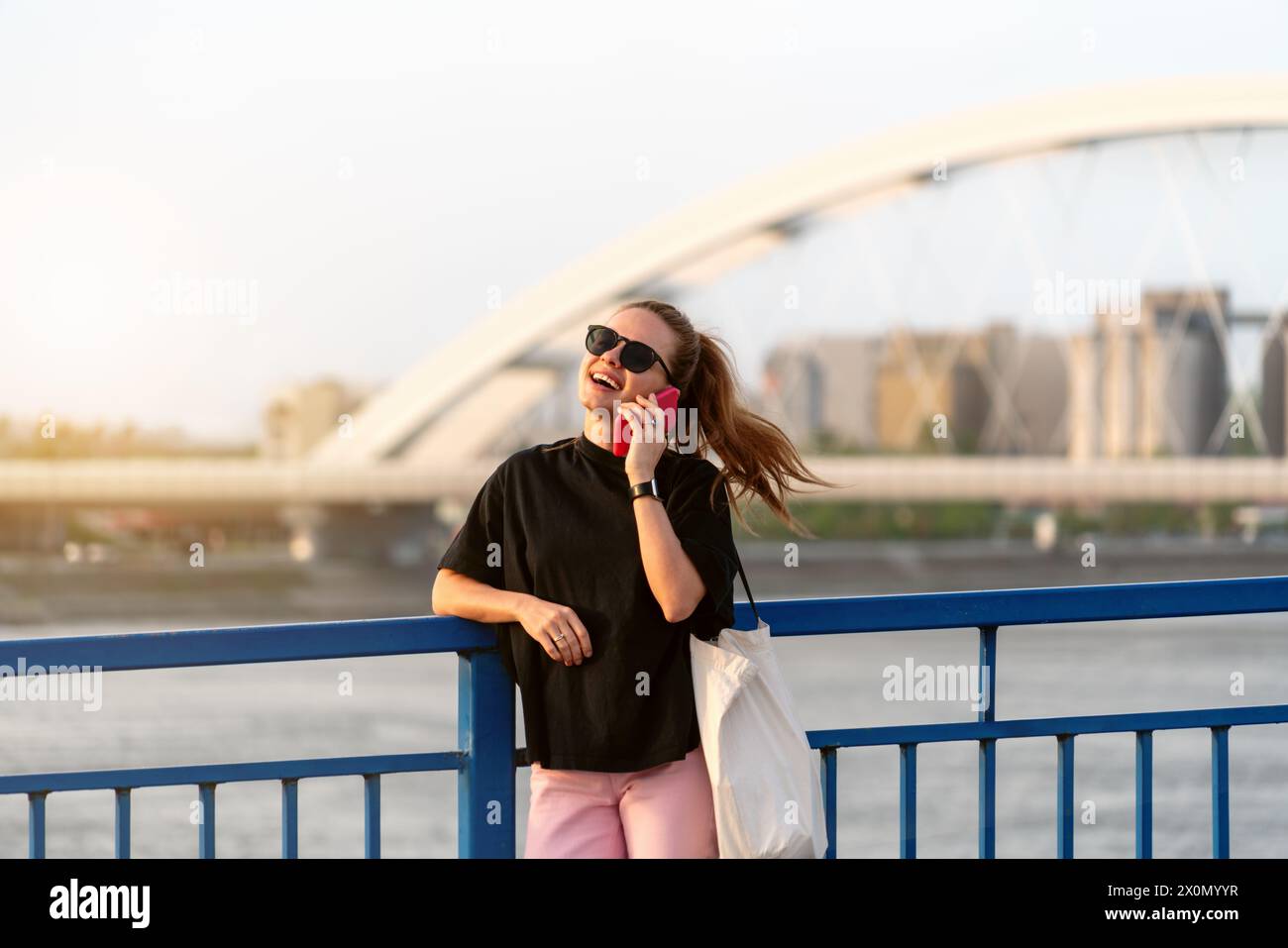 Una donna spensierata in città sta su un ponte e parla al telefono cellulare. Stile di vita cittadino. Foto Stock