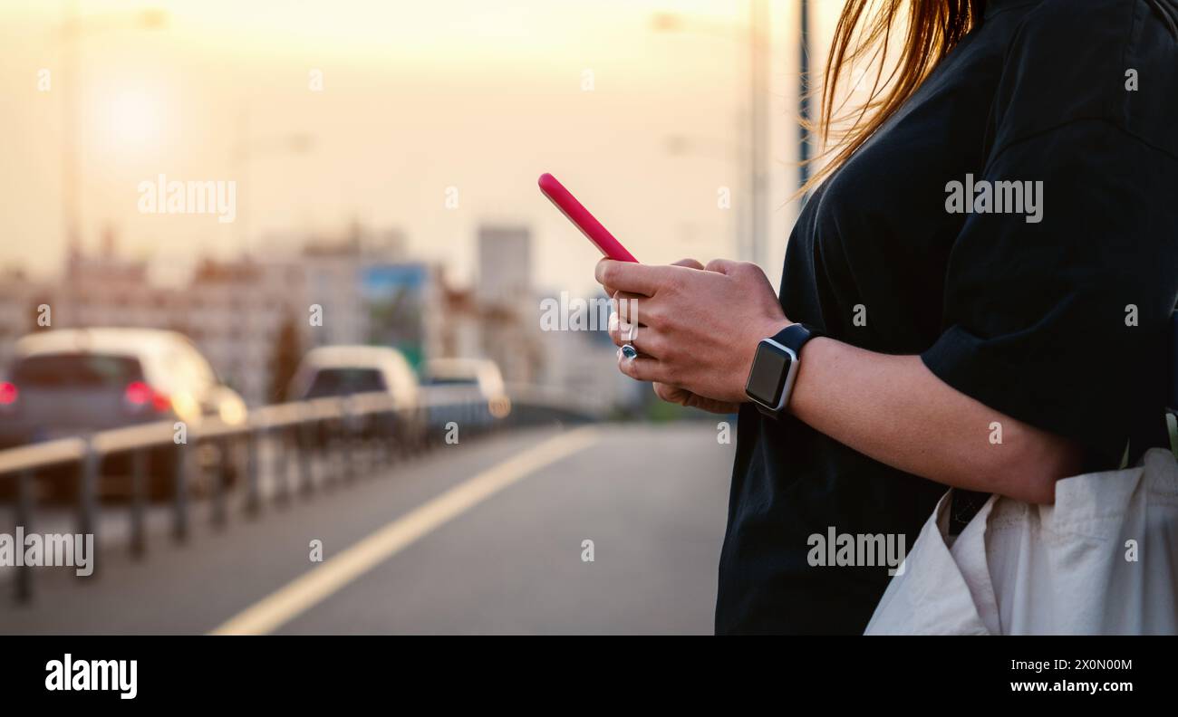Cellulare nella mano di una donna contro la città. Messaggistica online. Stile di vita cittadino. Foto Stock