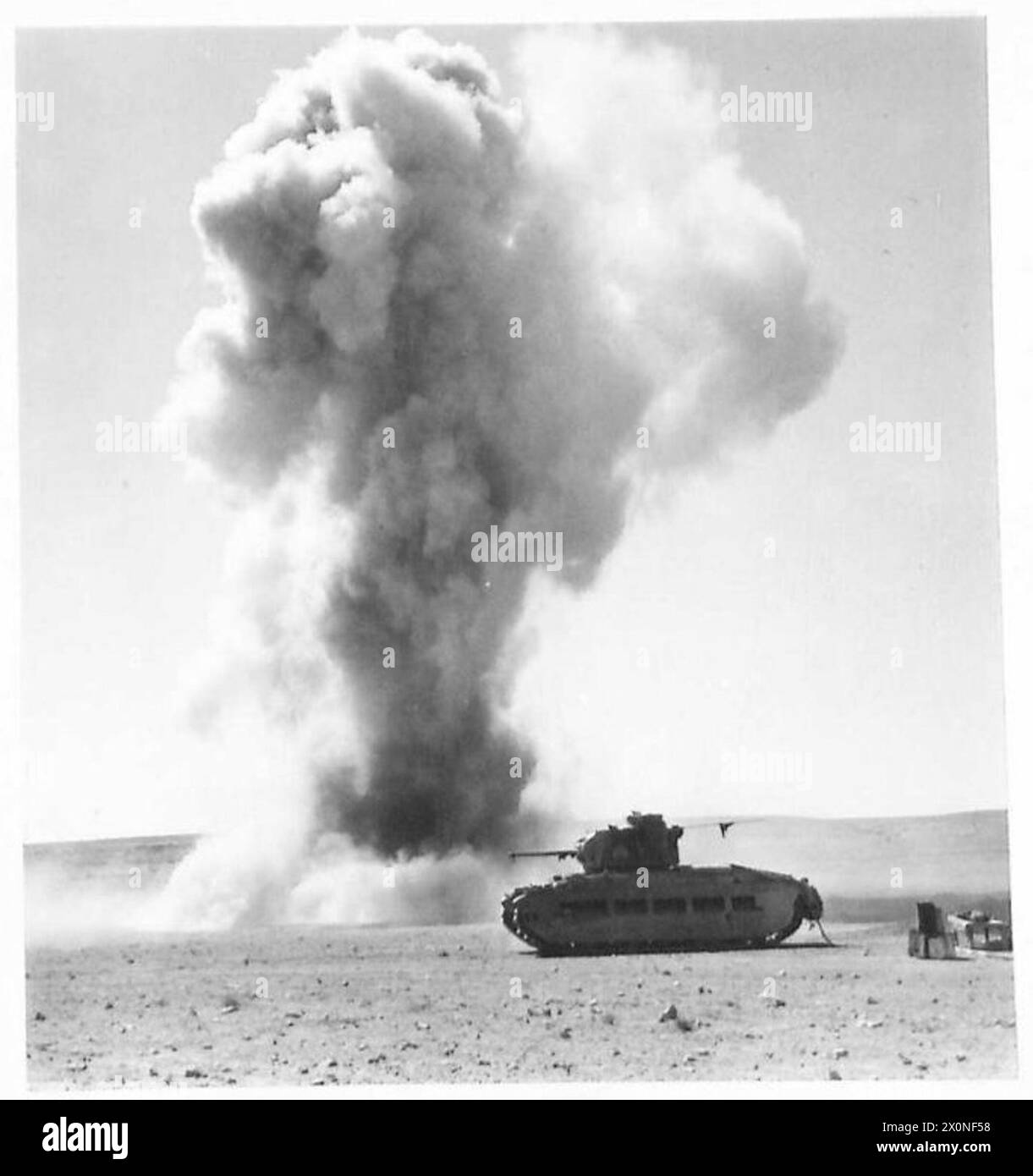 Un carro armato è posizionato mentre una bomba esplode nelle vicinanze, mostrando i preparativi per la creazione di pozzi di carri armati durante le operazioni militari. Foto Stock