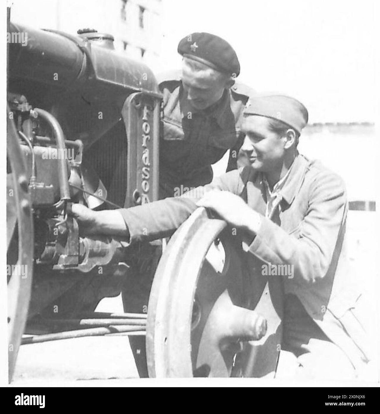 Fotografia di soldati jugoslavi che esaminano il motore di un trattore agricolo durante le operazioni di soccorso, sotto l'esercito britannico. Foto Stock