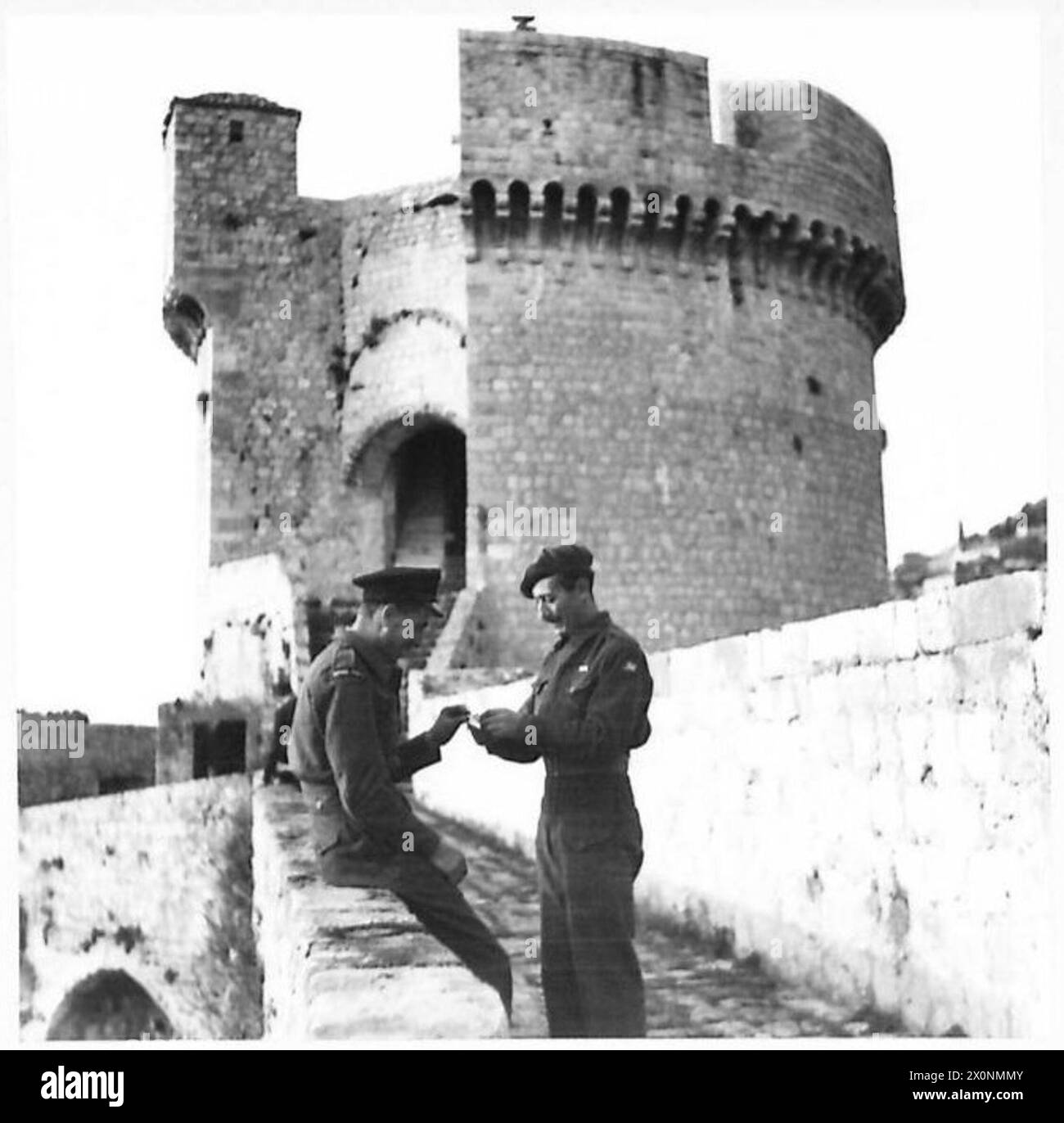 Due uomini si arrampicano sui vicoli stretti di Dubrovnik, Jugoslavia, e si fermano per una pausa sulle mura della città, illustrando il movimento urbano e il riposo durante le operazioni. Foto Stock