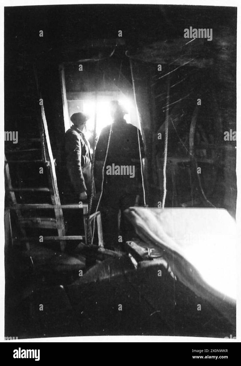 Fotografia di due soldati britannici che utilizzano un tradizionale mulino a vento olandese come punto di osservazione per individuare le posizioni nemiche in Olanda. L'immagine è un negativo fotografico del 21st Army Group. Foto Stock