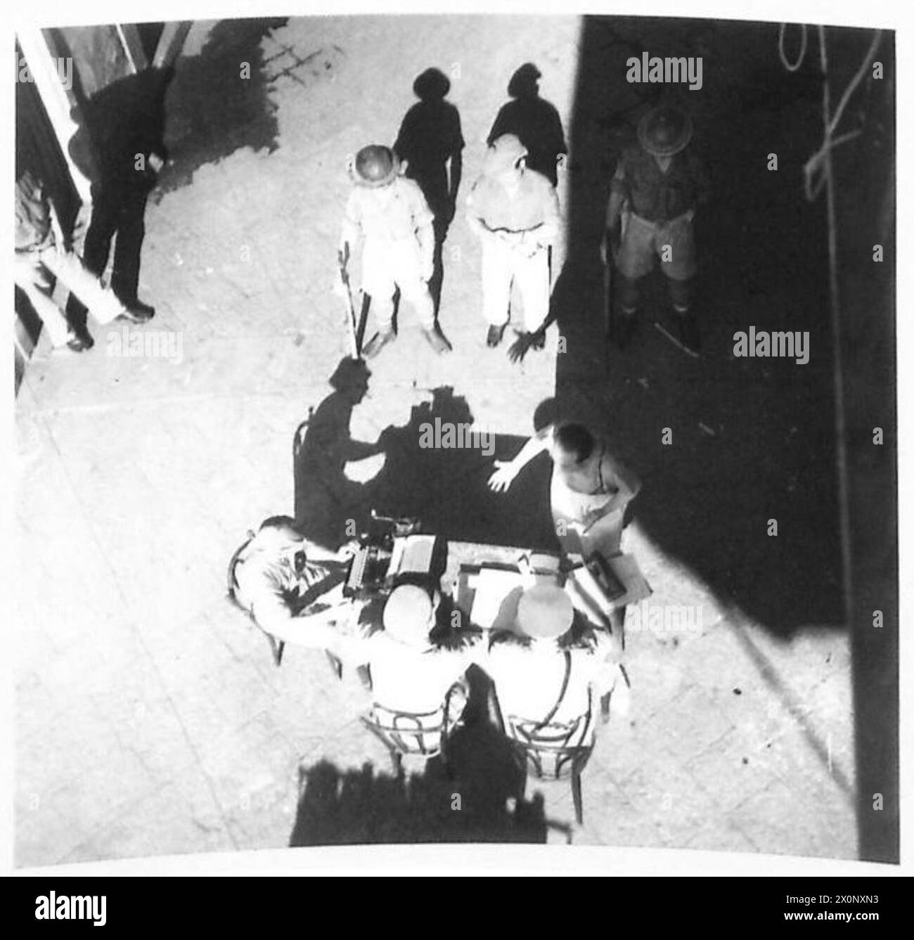 La fotografia mostra Desario Birancati, Vice Prefetto di Catania, sotto la guardia armata, che viene interrogato nel cortile di un ex quartier generale fascista in Sicilia. Foto Stock