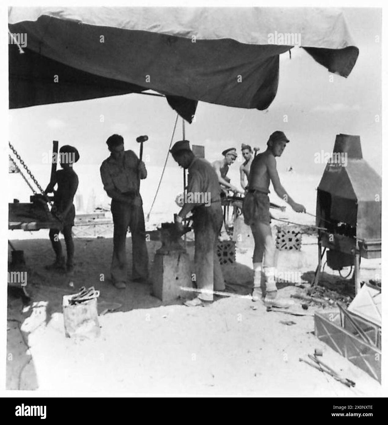 I fabbri vengono fotografati lavorando in laboratori nel deserto, resistendo al calore dei forni durante le operazioni di lavorazione dei metalli. Negativo fotografico dell'esercito britannico. Foto Stock