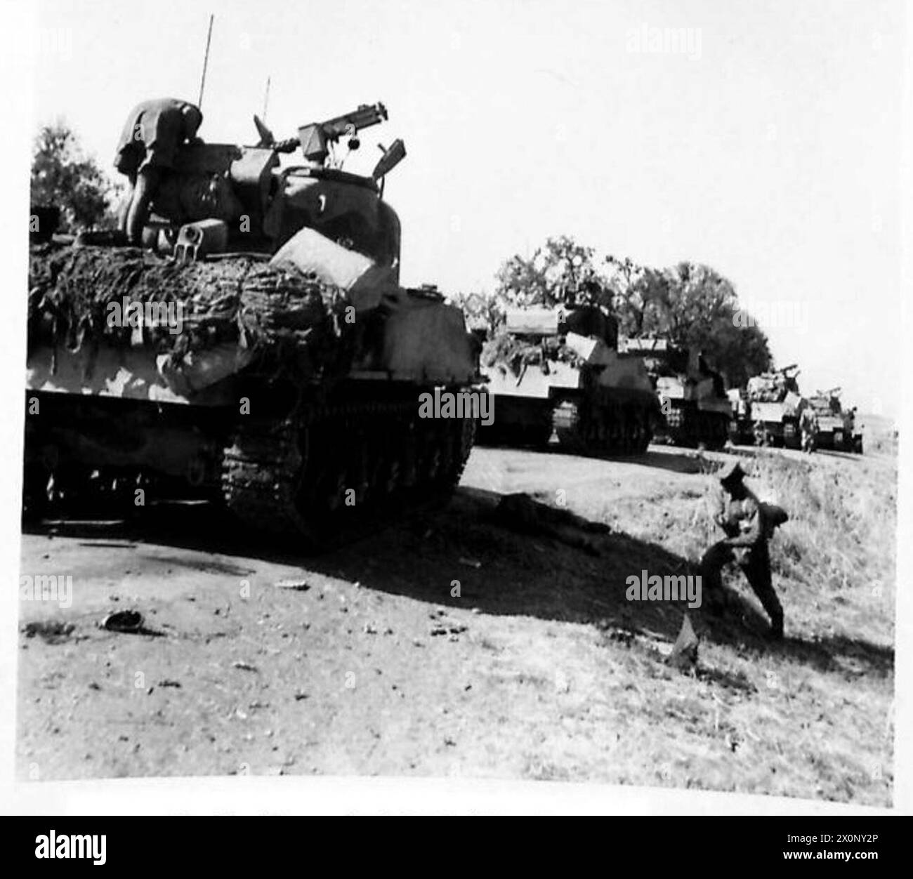 I carri Sherman avanzarono durante l'invasione della Sicilia, con un soldato caduto osservato accanto ai binari del carro. Foto Stock
