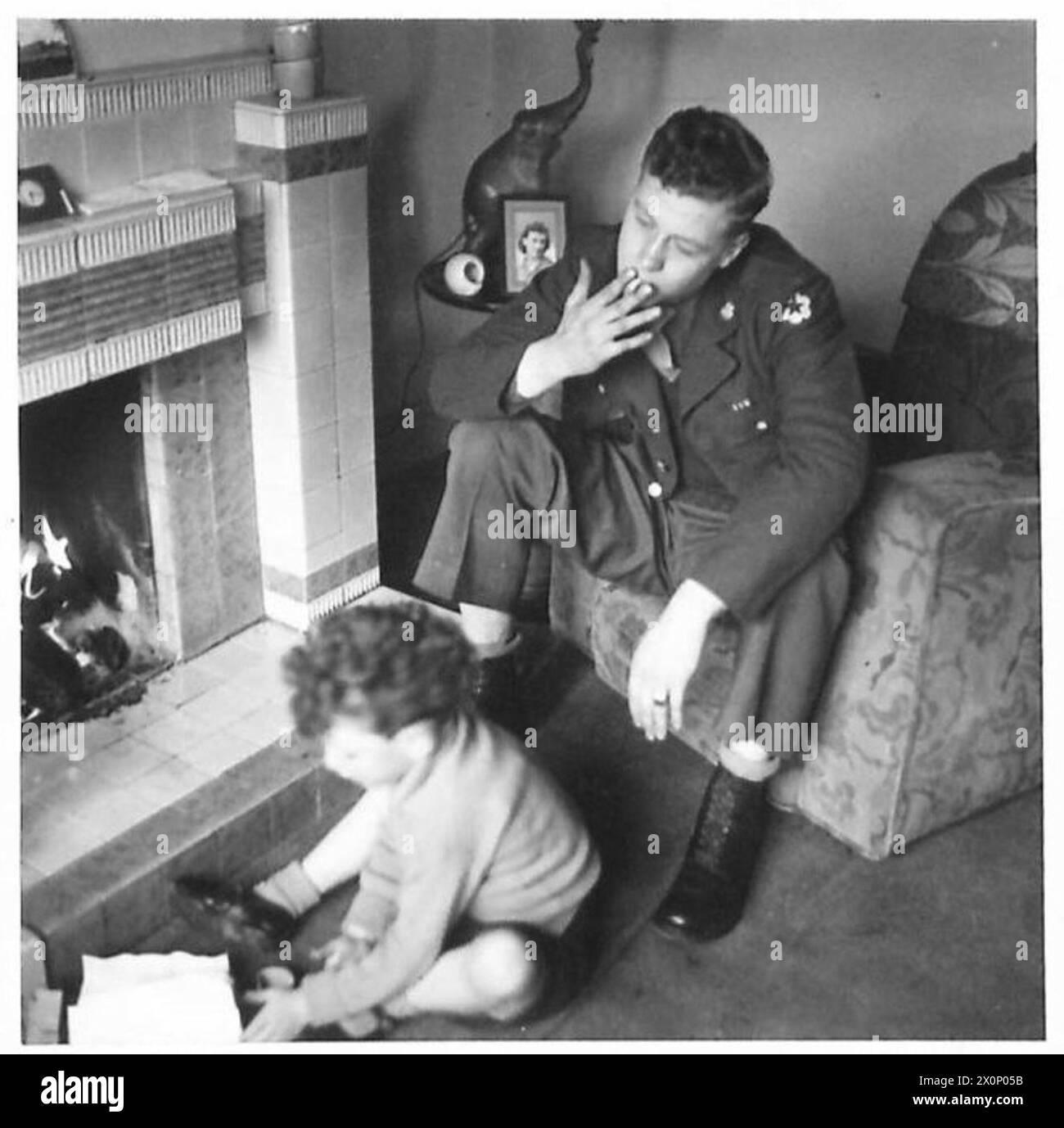 Un soldato dell'ottavo esercito britannico in congedo guarda un bambino giocare, riflettendo sulla propria casa negli Stati Uniti. La fotografia documenta il congedo delle truppe e i momenti personali durante la guerra. Foto Stock