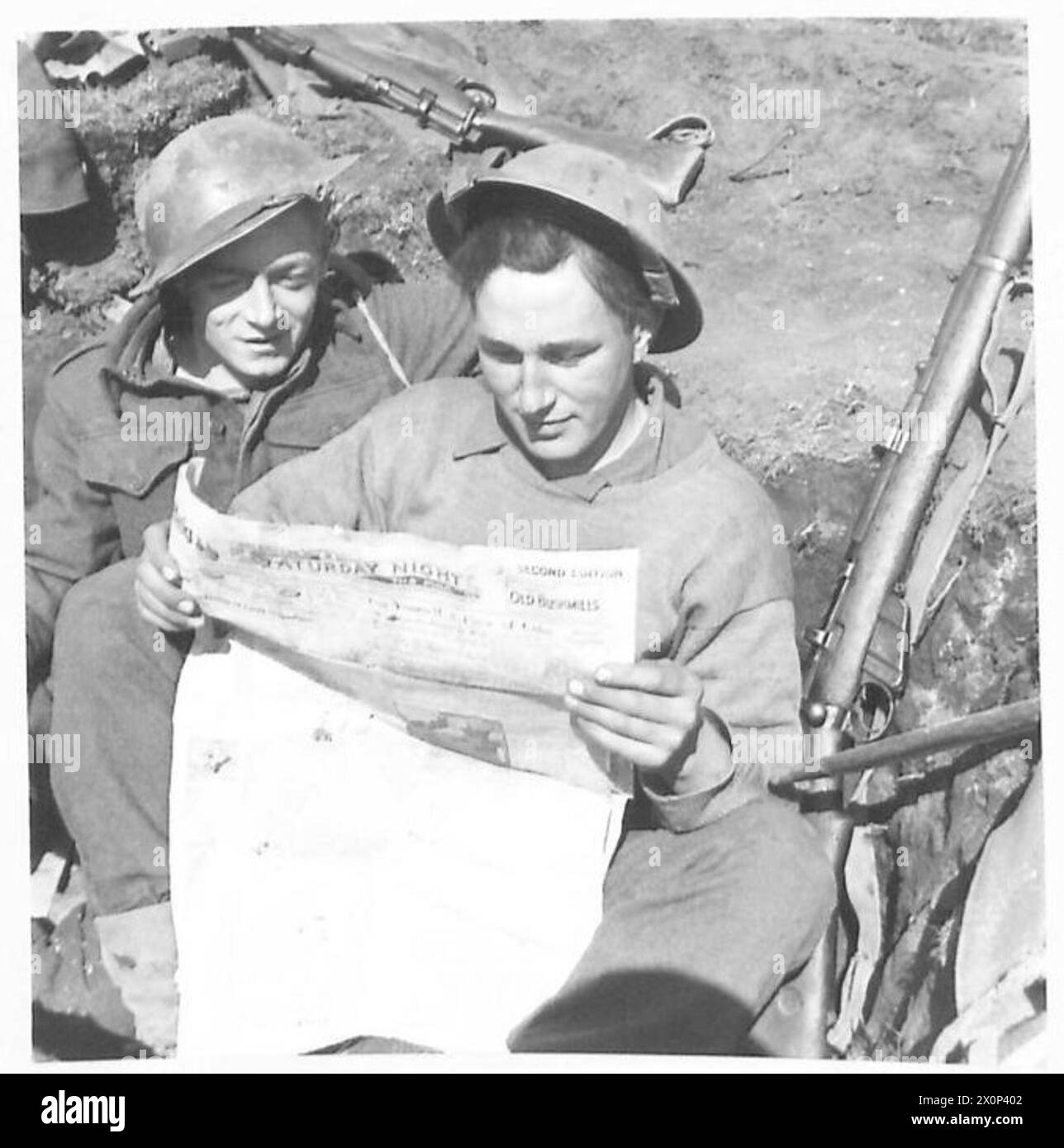 I soldati del battaglione irlandese Fusilier Clarke e Fusilier Hicky lessero un giornale di Belfast nella loro trincea in prima linea alla testa di ponte di Anzio durante le celebrazioni per il giorno di San Patrizio. Foto Stock
