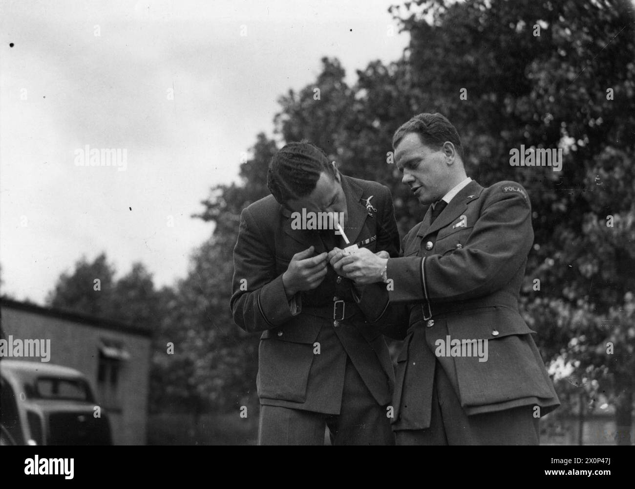 L'AERONAUTICA MILITARE POLACCA IN GRAN BRETAGNA, 1940-1947 - l'ufficiale pilota Jan "Donald Duck" Zumbach del No. 303 Polish Fighter Squadron riceve una luce dal pilota ufficiale Zygmunt Wodecki, ufficiale medico dello Squadrone, durante una pausa di sigarette. Fotografia scattata presso RAF Northolt o RAF Speke, luglio 1941 Polish Air Force, Polish Air Force, 303 "Kościuszko" Fighter Squadron, Zumbach, Jan Eugeniusz Ludwig, Wodecki, Zygmunt Foto Stock