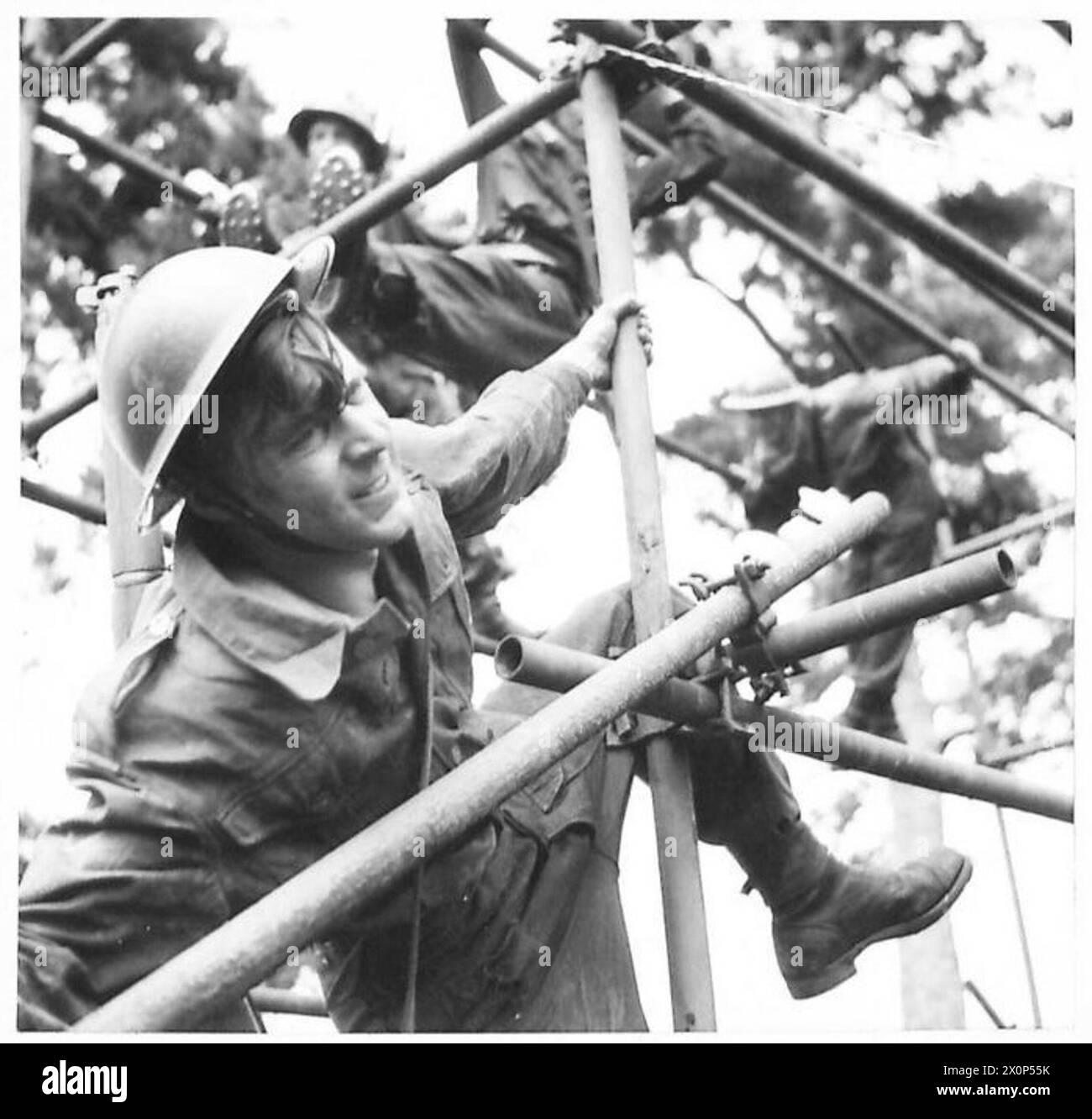 Fotografia che mostra un soldato che esegue un intenso esercizio fisico, arrampicandosi su ostacoli tubolari in acciaio come parte dell'addestramento militare. Foto Stock