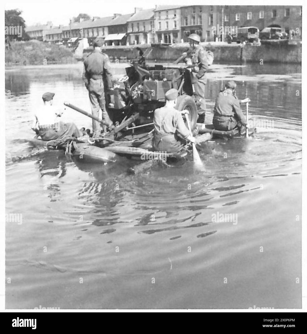 Il personale dell'esercito britannico attraversa un corpo d'acqua usando zattere improvvisate per trasportare i cannoni d'artiglieria. La fotografia documenta le operazioni ingegneristiche e logistiche in un ambiente sul campo. Foto Stock