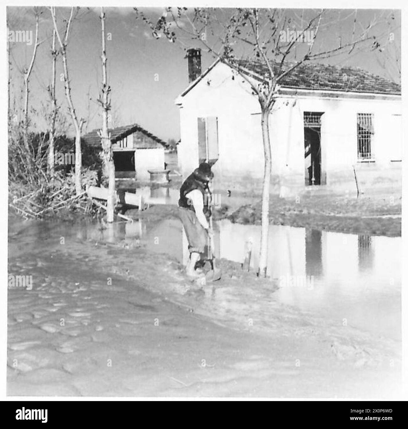Un residente italiano sgombra il fango dal percorso al suo cottage in seguito all'inondazione in un'area in cui è presente l'ottava Armata. Foto Stock
