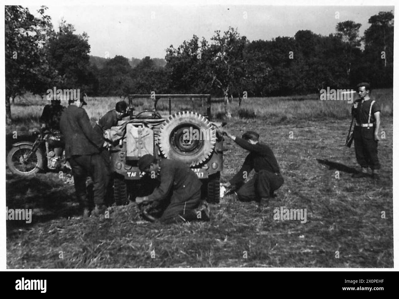Prigionieri catturati vicino a Conde sur Noireau in Normandia jeep e motociclette pulite mentre sono confinati vicino a una gabbia di prigionieri di guerra, illustrando la gestione dei prigionieri post-combattimento e la manutenzione dei veicoli. Foto Stock